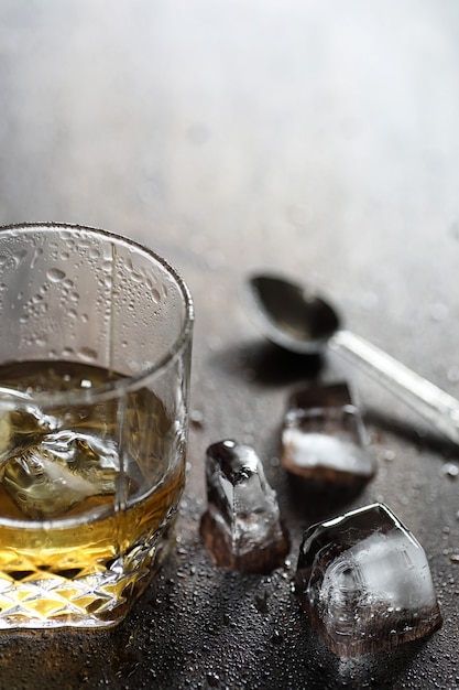 Whisky en un vaso y trozos de hielo sobre una mesa de madera