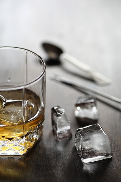 Whisky en un vaso y trozos de hielo sobre una mesa de madera