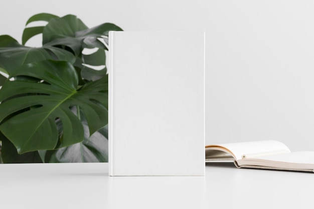 White-Book-Mockup mit Arbeitsplatzzubehör und einer Monstera-Pflanze