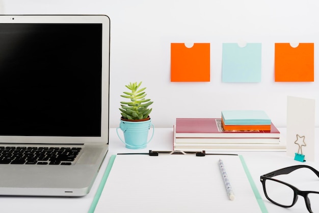 Wichtige Nachricht auf Zwischenablage und Laptop auf dem Schreibtisch mit Notizen Bücher Brille Blume und Bleistift wichtige Informationen auf dem Computerbildschirm und Notizblock auf dem Tisch