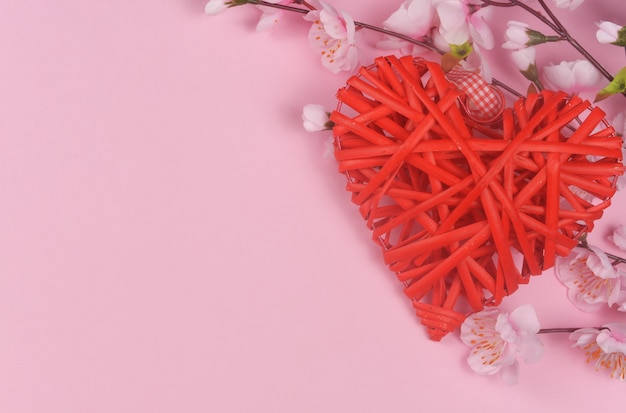 Wicker rotes Herz mit rosa Blumen auf einer rosa Oberfläche