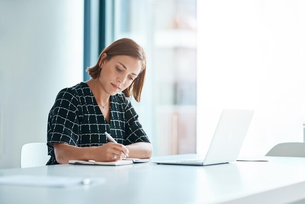 Widmungsstufe A plus Schnappschuss einer fokussierten jungen Geschäftsfrau, die in einem Büro auf einem Notizbuch schreibt