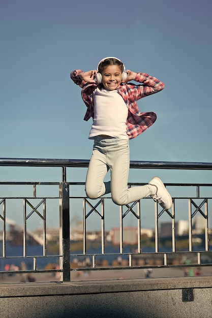 Wie ein Rockstar Kleines Mädchen, das zur Musik springt Kleines glückliches Kind, das Musik hört Kleines Kind, das die Musik spielt, die in den Kopfhörern spielt Netter Musikfan, der drahtlose Kopfhörer trägt