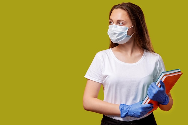 Wiedereröffnung der Schule Quarantänehygiene Besorgte Studentin in schützenden Gesichtsmaskenhandschuhen mit isolierten Büchern, die sich den grünen Kopierraum ansehen, der besorgt über den COVID19-Ausbruch der sozialen Distanzierung ist