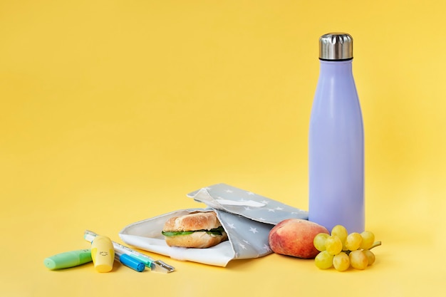 Wiederverwendbare Flasche und Sandwichverpackung auf leuchtend gelbem Hintergrund Nachhaltigkeitskonzept