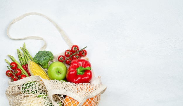 Wiederverwendbare Netztasche mit frischem Gemüse und Obst auf hellem Betonhintergrund