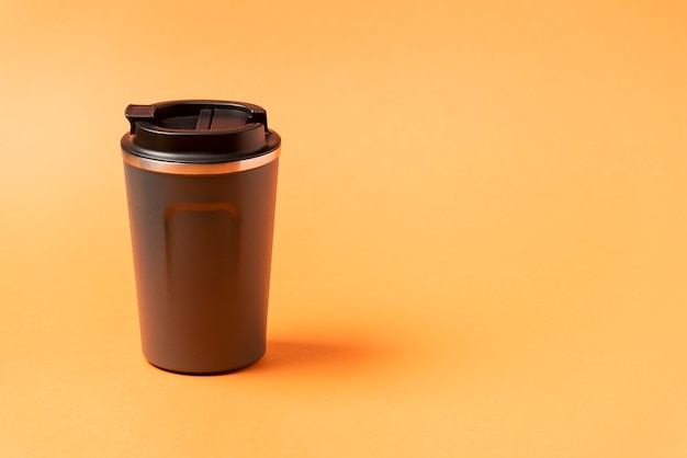 Wiederverwendbarer Becher, Reise-Kaffeebecher aus Kunststoff zum Mitnehmen. Plastikbecher mit Silikonhalter auf natürlichem orangefarbenem Hintergrund.