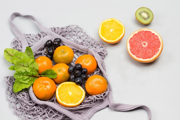 Foto wiederverwendbarer netzbeutel mit früchten, tangerinen, grapefruit, kiwi-trauben und kartoffelblättern auf dem tisch