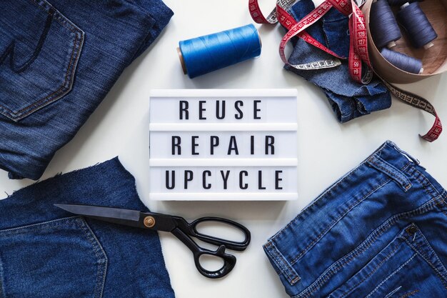 Wiederverwendung von Reparatur-Upcycle-Text auf Lichttafel auf Nähmaschinen-Hintergrundstapel alter Jeans-Denim