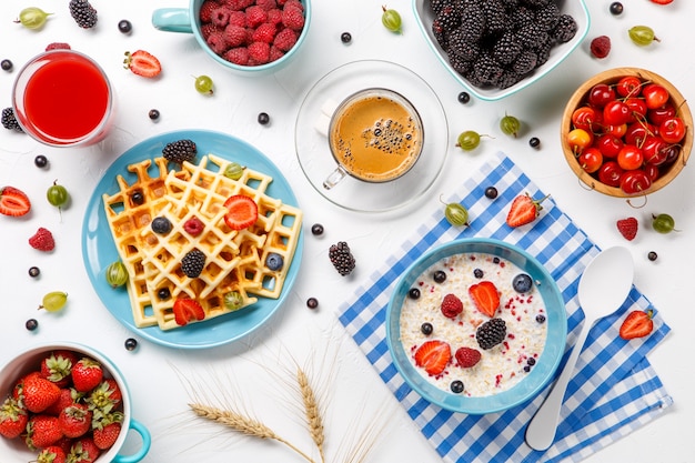 Wiener Waffeln, Haferflocken, Kaffee, Himbeeren, Erdbeeren und Stachelbeeren auf einem weißen Tisch