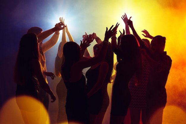 Wild. Eine Menschenmenge in Silhouette hebt ihre Hände auf der Tanzfläche auf Neonlichthintergrund. Nachtleben, Club, Musik, Tanz, Bewegung, Jugend. Gelb-blaue Farben und bewegende Mädchen und Jungen.