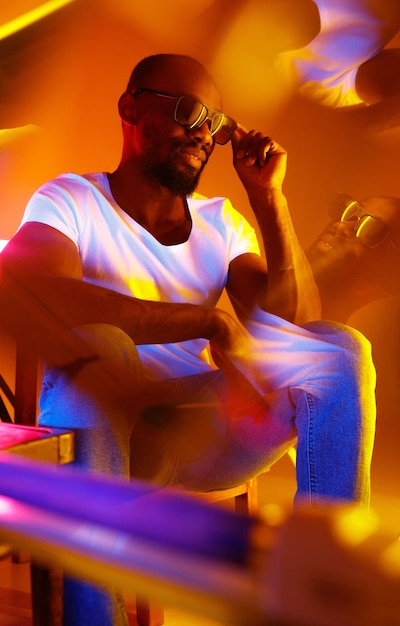 Wild. Filmisches Porträt eines stilvollen jungen Mannes im neonbeleuchteten Raum. Helle Neonfarben. Afroamerikanisches Modell, Musiker drinnen. Jugendkultur im Party-, Festival- und Musikkonzept.