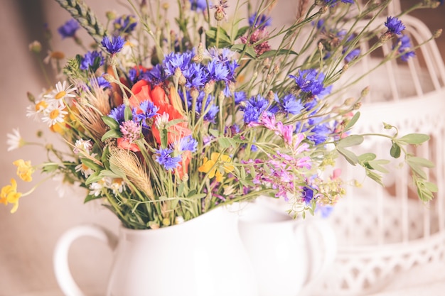 Wildblumen in weißer Keramikkanne und Tassen auf Tablett