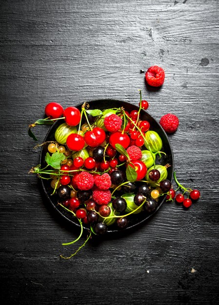 Wilde Beeren in der alten Platte auf schwarzem Holztisch.