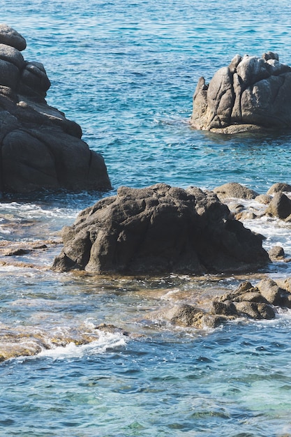 Wilde felsige Strandküste und die Meereswelle spritzt auf Felsen im ruhigen Meer der Küste Brechende Wellen zu den Felsen am Ufer erzeugen weißen Meeresschaum