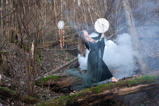 Foto wilde frau spielt schamanische trommeln auf einem grünen moosstamm im wald weiße rauchbombe