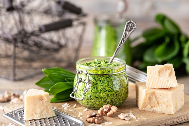 Wildes Lauchpesto mit Olivenöl und Parmesankäse in einem Glas auf einem Holztisch. Nützliche Eigenschaften von Ramson. Blätter von frischem Bärlauch.