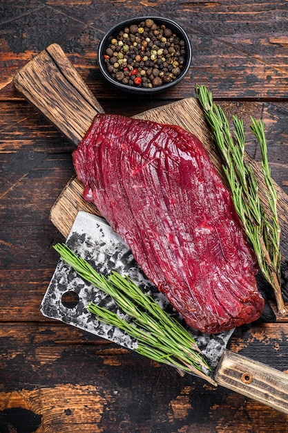 Wildes rohes Fleischsteak auf einem Schneidebrett mit Rosmarin. Schwarzer Hintergrund. Ansicht von oben.