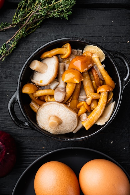 Wildpilze boletus edulis und kappenboletus in einem gefäßsatz, auf schwarzem holztischhintergrund, draufsicht flach liegen