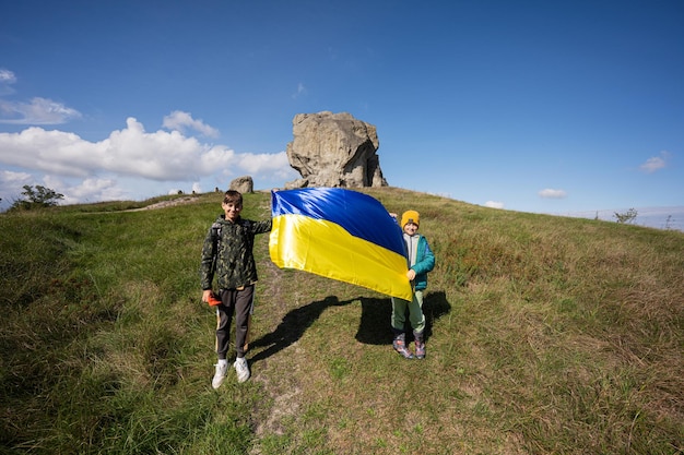 Willkommen in der Ukraine Zwei Brüder halten die ukrainische Flagge in der Nähe eines großen Steins auf dem Hügel Pidkamin