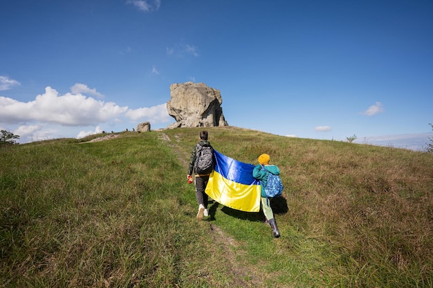 Willkommen in der Ukraine Zwei Brüder halten die ukrainische Flagge in der Nähe eines großen Steins auf dem Hügel Pidkamin