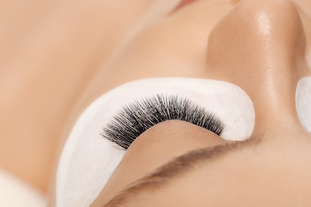 Wimpernverlängerungen. Falsche Wimpern. Wimpernverlängerungsverfahren. Schließen Sie das Porträt des Frauenauges mit langen Wimpern. Professionelle Stylistin verlängert weibliche Wimpern. Meister und Kunde im Schönheitssalon.