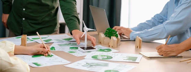 Windmühle-Modell repräsentierte erneuerbare Energie und Holzblock repräsentierte Öko-Stadt wurde auf einen grünen Geschäftstisch mit umweltbezogenen Dokumenten verstreut herum platziert Frontansicht