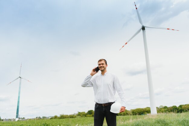 Windmühleningenieur, der am Telefon auf Windmühle spricht. Ein Mann in einem Helm überwacht den Betrieb der elektrischen Windmühlen.