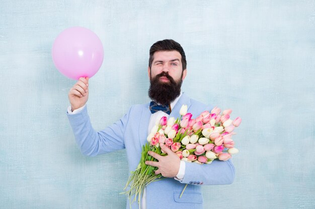 Wink geben Glücklicher Junggeselle halten Blumen und Ballon Tulpenblumenstrauß für Dating-Jubiläum Valentinstag Frauentag Jubiläumsfeier Geburtstagsjubiläum Ich wünsche alles Gute zum Jubiläum