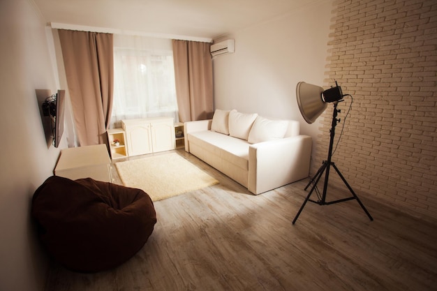 Winkelansicht des gestalteten Wohnzimmers in hellen Pastellfarben Fenster mit Vorhängen weißes Sofa Holzboden Heimstudio für Familienfotosessions mit Studiobeleuchtung