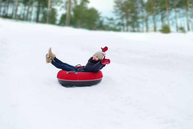 Winter-, Freizeit-, Sport- und People-Konzept - glückliches Teenager-Mädchen oder Frau, die auf der Schneeröhre herunterrutscht
