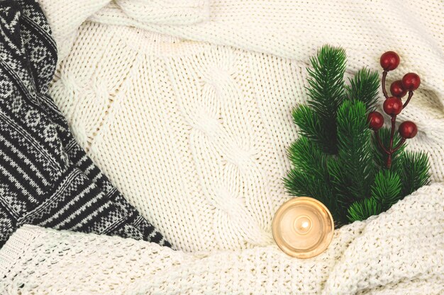 Winter gemütlicher Hintergrund, Woll- und Strickpullover, Tannenzweig mit roten Beeren und Kerze, Komposition mit Kopierraum. Foto in hoher Qualität