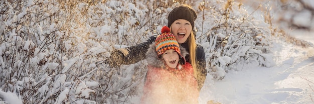 Winter-Mutter und Sohn werfen Schneeball in die Kamera und lächeln glücklich, Spaß im Freien zu haben, wenn es schneit