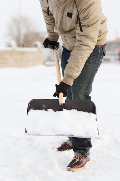 Winter- und Reinigungskonzept - Nahaufnahme eines Mannes, der Schnee von der Auffahrt schaufelt