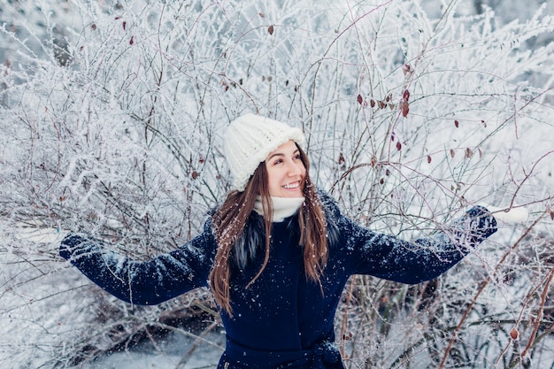 Foto winteraktivitäten. junge frau, die niederlassungen mit reif und schnee im winterwald rüttelt. mädchen, das spaß draußen hat.