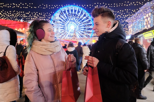 Wintereinkäufe, Weihnachtsrabatte und Geschenke, ein paar Teenager mit Einkaufstüten auf dem Stadtmarkt, Girlandenlichter des abendlichen Stadthintergrunds