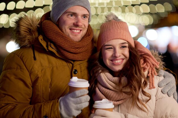 Foto winterferien heiße getränke und menschen konzept glückliches junges paar mit kaffee über weihnachtslichtern am abend