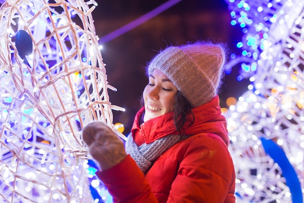 Winterferienzeit. Weihnachten, Neujahrskonzept. Lustige glückliche Frau verbringen Zeit damit, Spaß in der Nähe von beleuchteten und dekorierten Schaufenstern auf der Stadtstraße zu haben.
