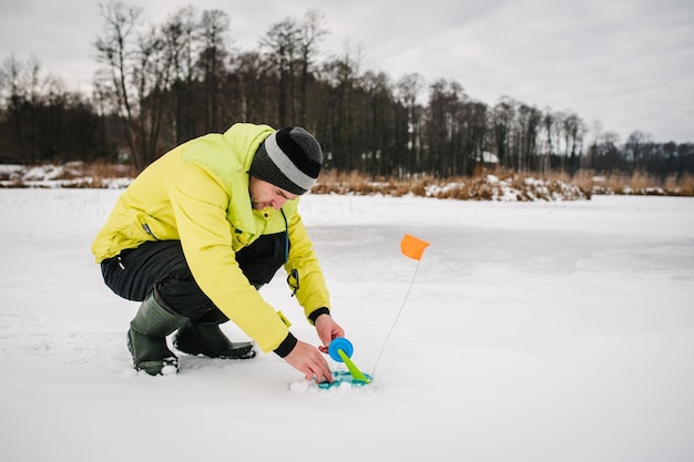 Winterfischen auf Hecht auf dem nachgemachten Fisch auf dem zugefrorenen See Fischer stellen kleine Ausrüstung für das Winterfischen auf dem Teich auf Eisfischer, der einen Fisch einholt