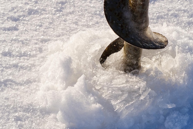 Winterfischereikonzept Fischer, der das Loch im Eis durch Eisschraube macht