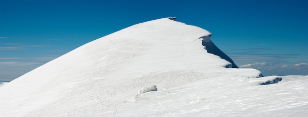 Wintergebirgskamm mit überhängenden Schneekappen und Snowboardspuren auf blauem Himmel