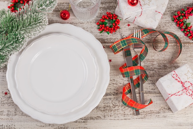 Wintergedeck mit Weihnachts- und Neujahrsdekorationen auf weißem Holztisch. Festliche Tischdekoration zum Weihnachtsessen.