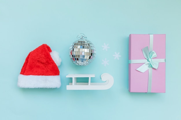 Wintergegenstände verzieren Weihnachtsmützenschlitten-Geschenkbox lokalisiert auf blauem Hintergrund
