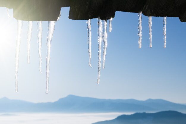 Winterhintergrund mit Eiszapfengrenze. Sonniges Wetter mit blauem Himmel und Berggipfeln
