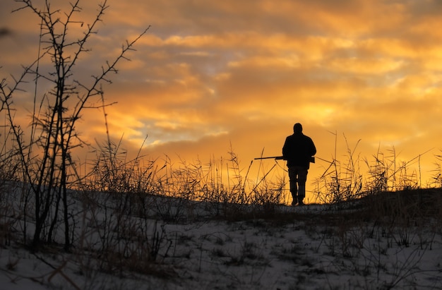 Winterjagd bei Sonnenaufgang. Jäger bewegt sich mit Schrotflinte und sucht nach Beute.