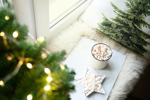Winterkaffee mit Marshmallow auf gemütlicher Fensterbank mit Weihnachtsbaum