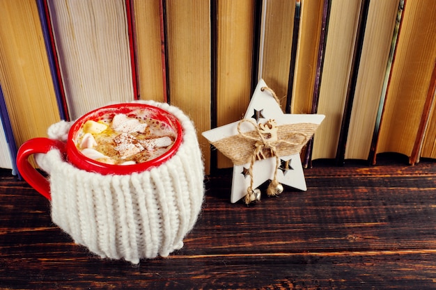 Winterkaffeegetränk, Kakao mit Schlagsahne und Eibische in einer roten Keramikschale. Stehend im Bücherregal, in der Nähe des Weihnachtssterns.