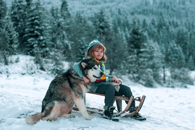 Winterkind kleiner Junge, der Spaß mit heiserem Hund im Schnee hat