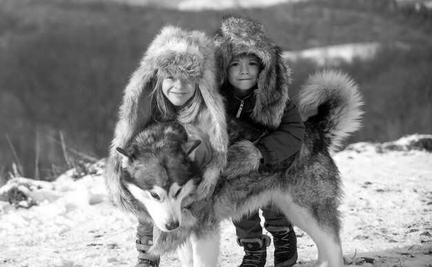 Winterkinder umarmen Husky im Schnee im Winterwald