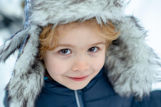 Winterkindgesicht hautnah. Glückliches Kind, das auf einem verschneiten Winterspaziergang mit Schnee spielt. Schöne Winterzeit.